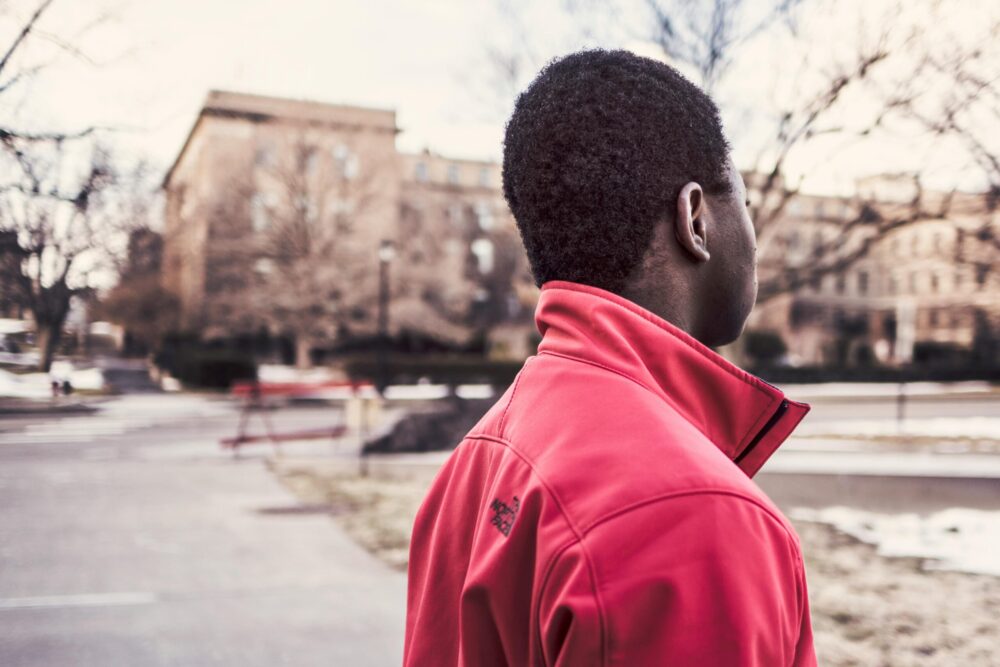 Black teenage boy on a City street, facing away from the camera. (Photo by Gratisography via Pexels)
