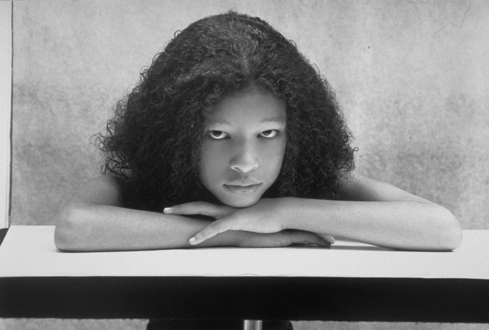 Black and white photo of a young girl with her head resting on her arms.