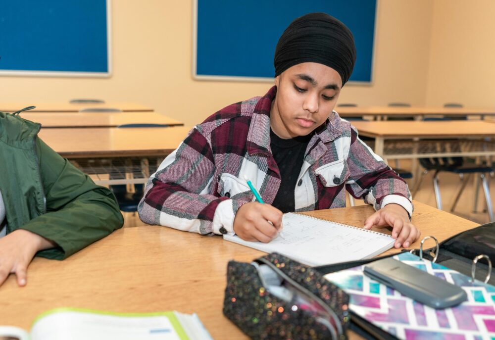 Teenager sits in a classroom doing schoolwork. (Photo by World Sikh Organization of Canada via Pexels)