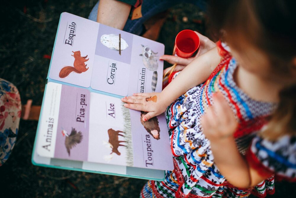 Child reading a picture book in Portuguese with a parent. (Photo by Helena Lopes via Pexels)