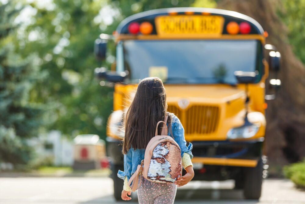 Young girl wearing a sparkly backpack walks towards a school bus. (Photo by Angelov, Adobe Stock)
