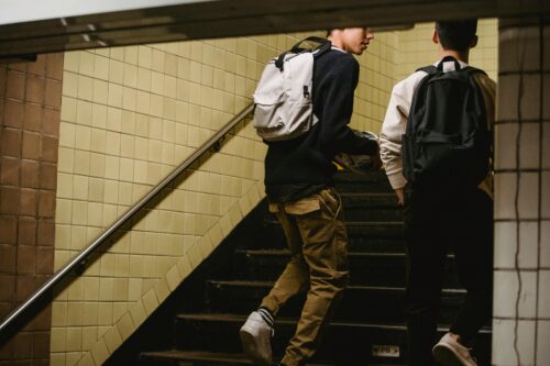 Two teenage boys wearing backpacks climb the stairs in the subway. (Photo by Armin Rimoldi from Pexels)