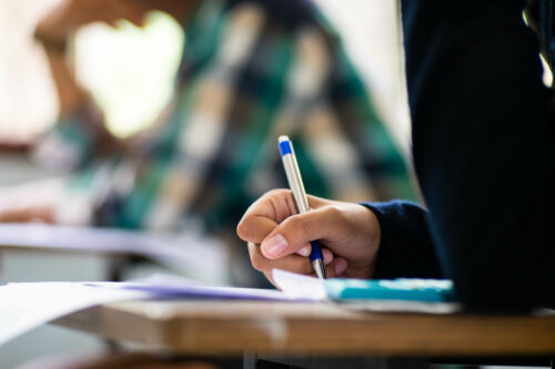 Close up of students writing on exam answer sheets in a classroom. (Photo by arrowsmith2, Adobe Stock)