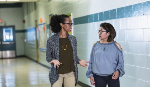 Two teachers walking and talking in a school hallway. (Photo by kali9, iStock)