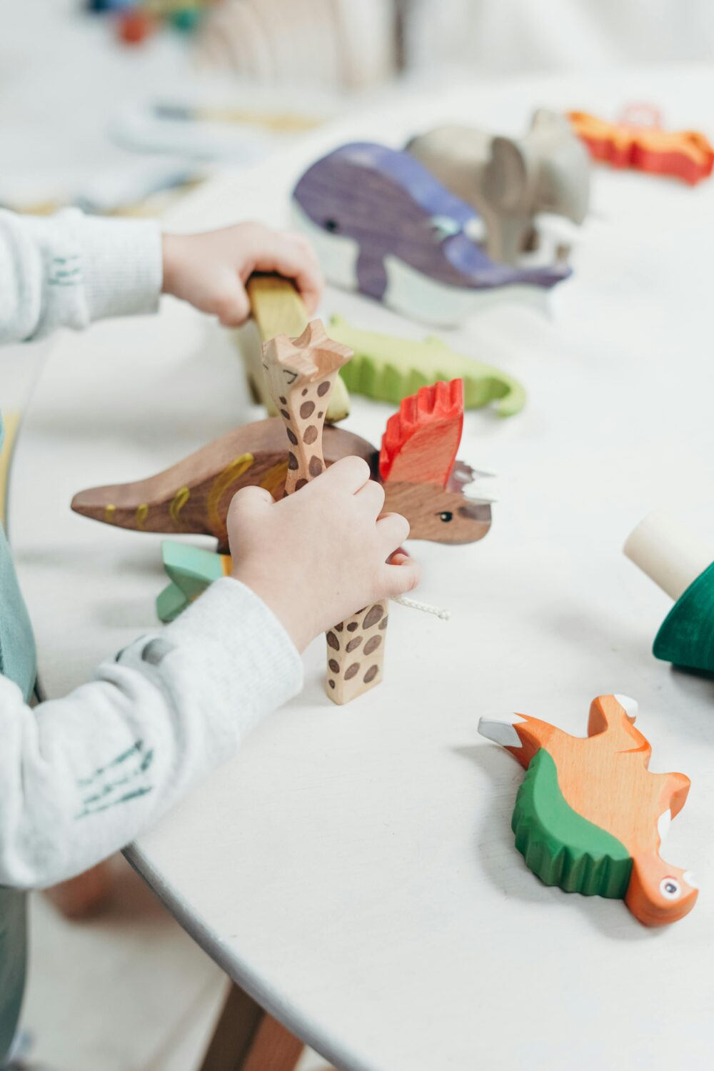 Hands of a toddler playing with wooden animals and dinosaurs. (Photo by cottonbro studio via Pexels)