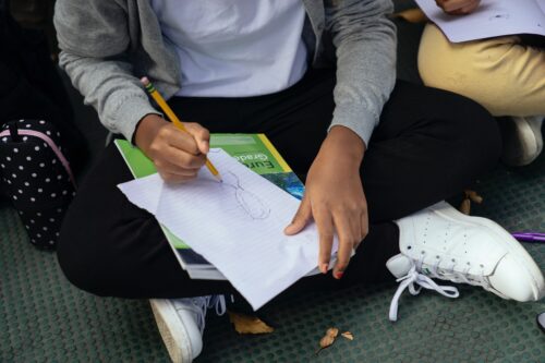 Midsection of a girl sitting on the ground doing schoolwork. (Photo by Mary Taylor via Pexels)
