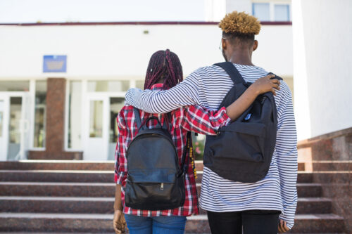 Two teenagers walk up the steps of a school, arms around one another. (Image by Freepik)