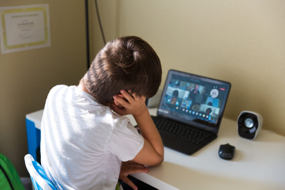 Elementary school student, viewed from behind, having a video call with classmates. (Photo by Tinatin, Adobe Stock)