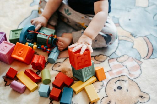 A toddler sits on the floor with legos and blocks. (Photo by Lisa Fotios from Pexels)