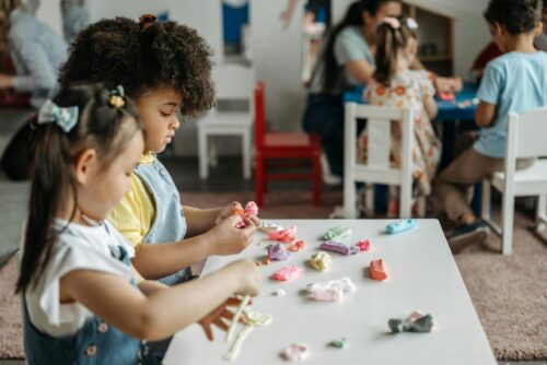 Two preschoolers play with clay at a small table.