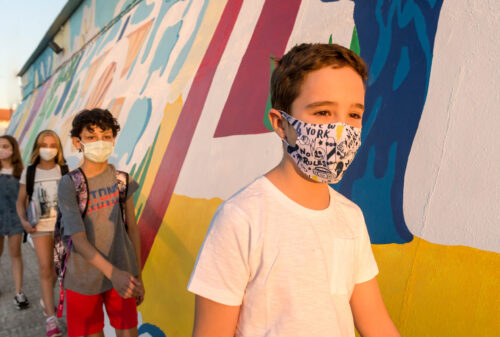 Row of children with protective masks walk with social distance to enter the school.