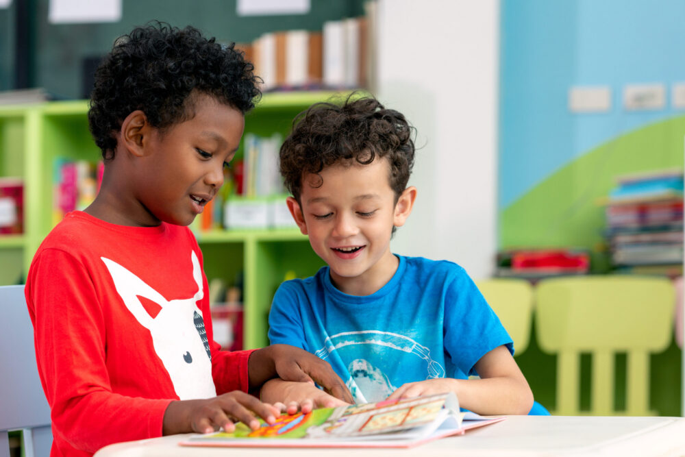 Two preschool boys reading a book together in a classroom. (Photo by anekoho, Adobe Stock)