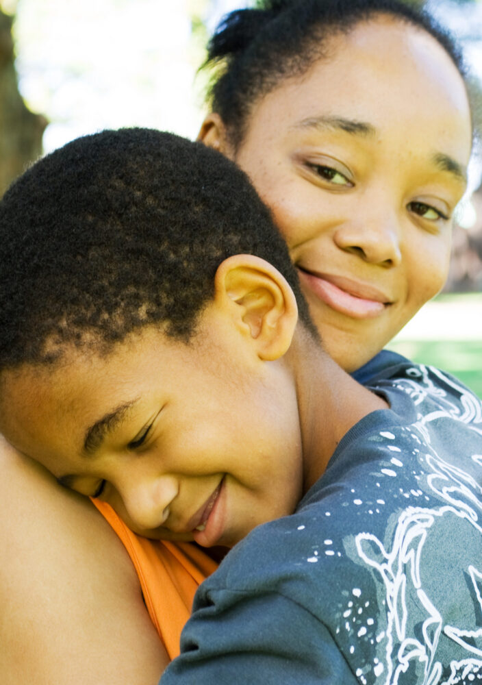 A woman smiles at the camera while hugging a young boy.