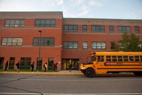 Students line up on socially distanced dots painted on the sidewalk to wait their turn to have their temperatures checked before entering Middletown High School.
