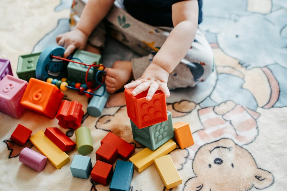 A toddler sits on the floor with legos and blocks. (Photo by Lisa Fotios from Pexels)