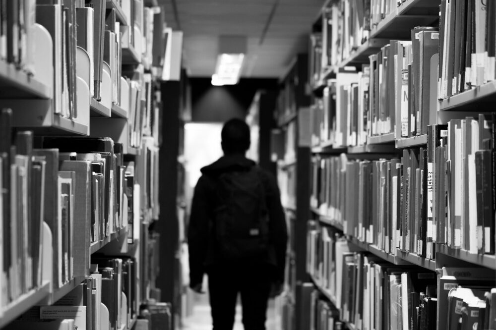 Silhouette of a male student walking down a row of books in a library.