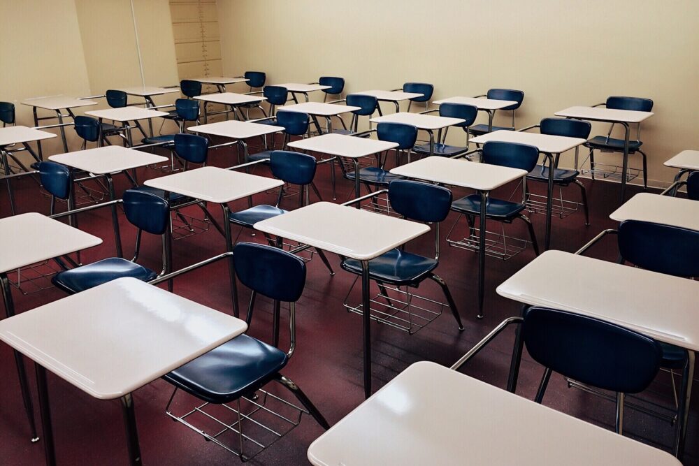 Desks in an empty classroom. (Image by WOKANDAPIX from Pixabay)