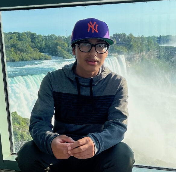 anselmo in front of niagra falls, wearing a purple yankees cap and glasses