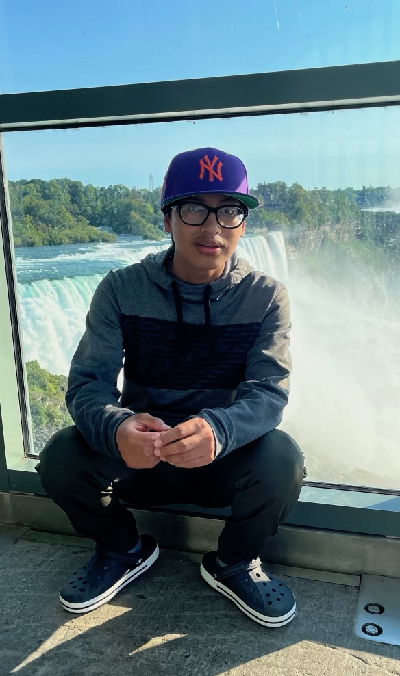 anselmo in front of niagra falls, wearing a purple yankees cap and glasses