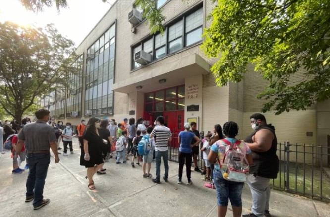 Several parents and their children wait outside of a school building before the start of Summer Rising in 2021. This year’s program will serve 110,000 children.