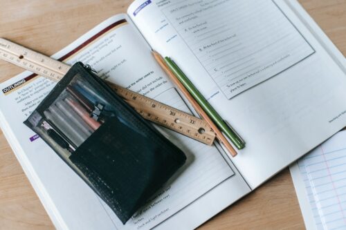 A ruler, pencil, and pens sitting on an open textbook. (Photo by Katerina Holmes from Pexels)
