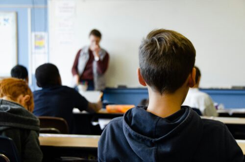 Rear view of a boy wearing black hoodie sitting in a classroom. (Photo by Taylor Flowe on Unsplash)
