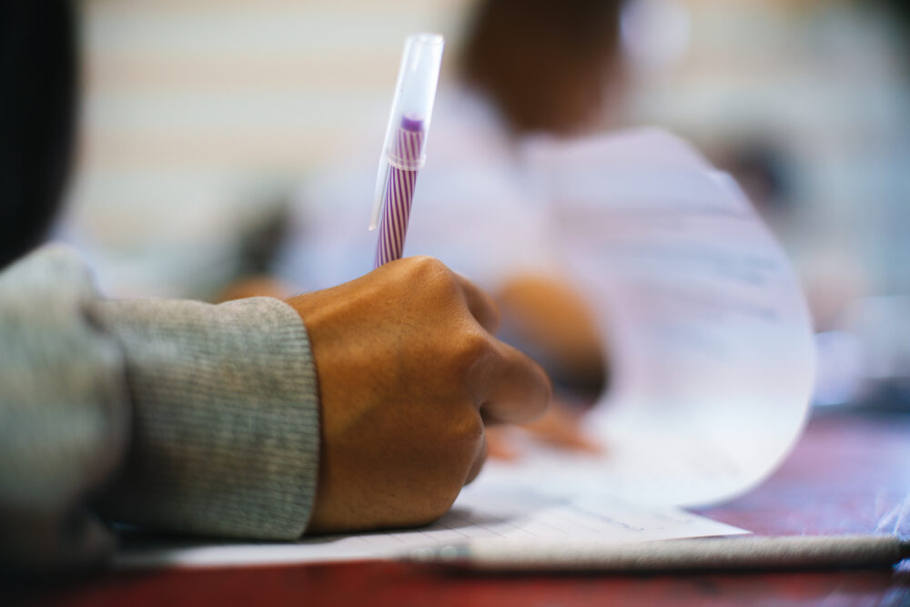 Student writing on exam papers in a classroom. (Photo by arrowsmith2, Adobe Stock)