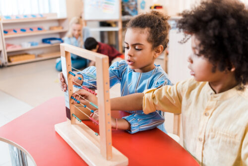 Selective focus of two children playing with scores with teacher and child at background. (Photo by Lightfield Studios, Adobe Stock.)