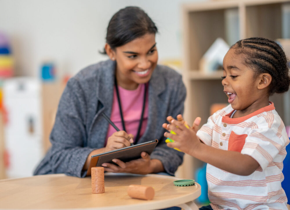 A female occupational therapist works with a young boy, using play-doh to work on the boy's gross motor skills. (Photo by FatCamera, iStock)