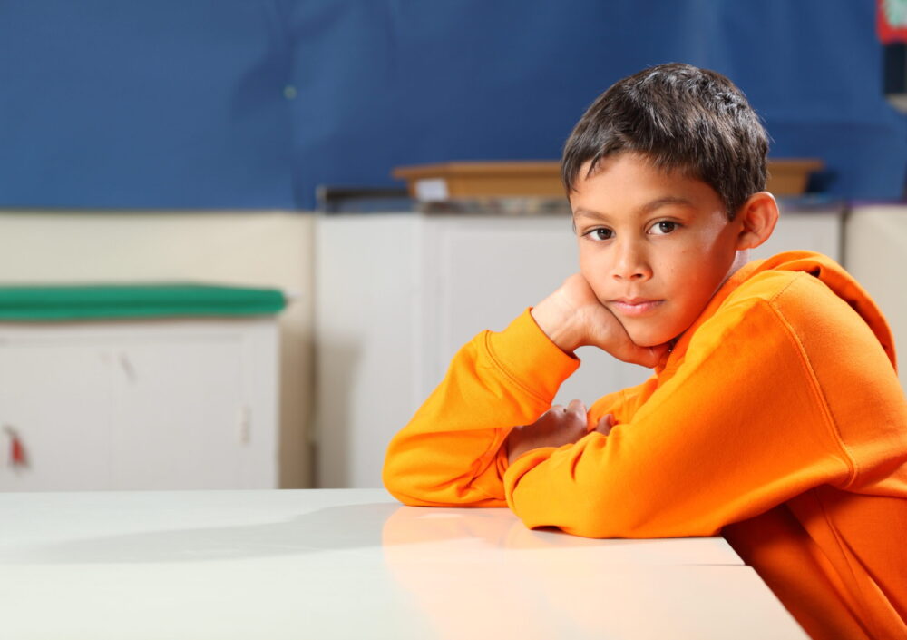 Young boy sits in a classroom, looking at the camera