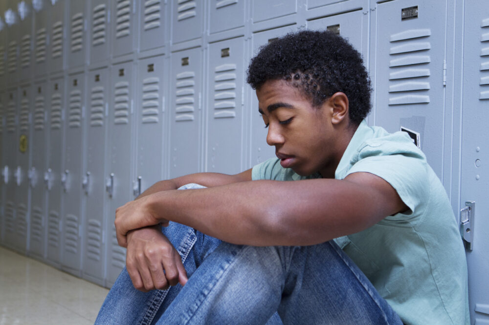 Boy sits alone in a school hallway, his back against the lockers