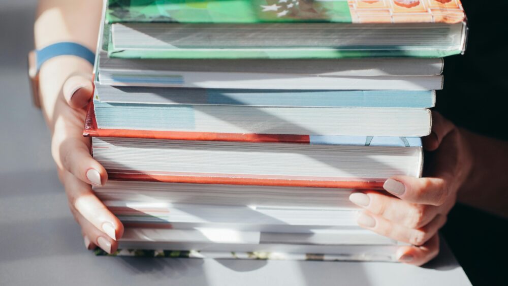 Close-up on person holding a stack of textbooks. (Photo by Kindel Media via Pexels)