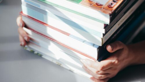 Close-up on person holding a stack of textbooks.