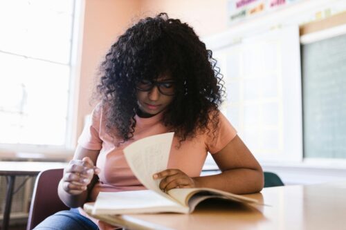 Teen girl flips through a book in a classroom. (Photo by RDNE Stock Project via Pexels)
