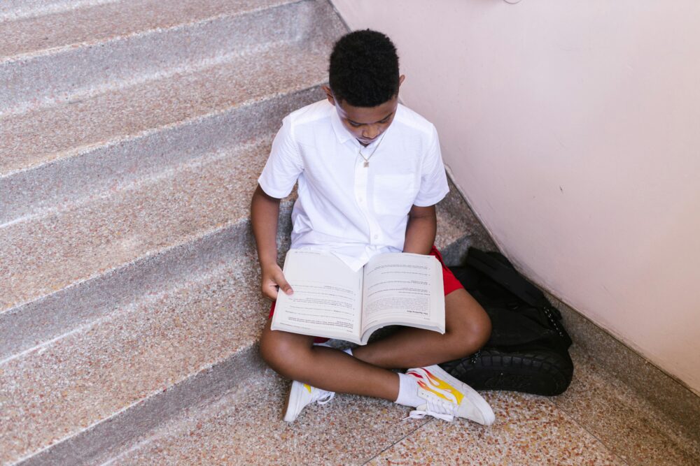 Boy sits in the stairwell of a school, looking at a textbook. (Photo by RDNE Stock Project via Pexels)