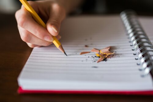 Person holding pencil writing on notebook. (Photo by Thought Catalog on Unsplash)