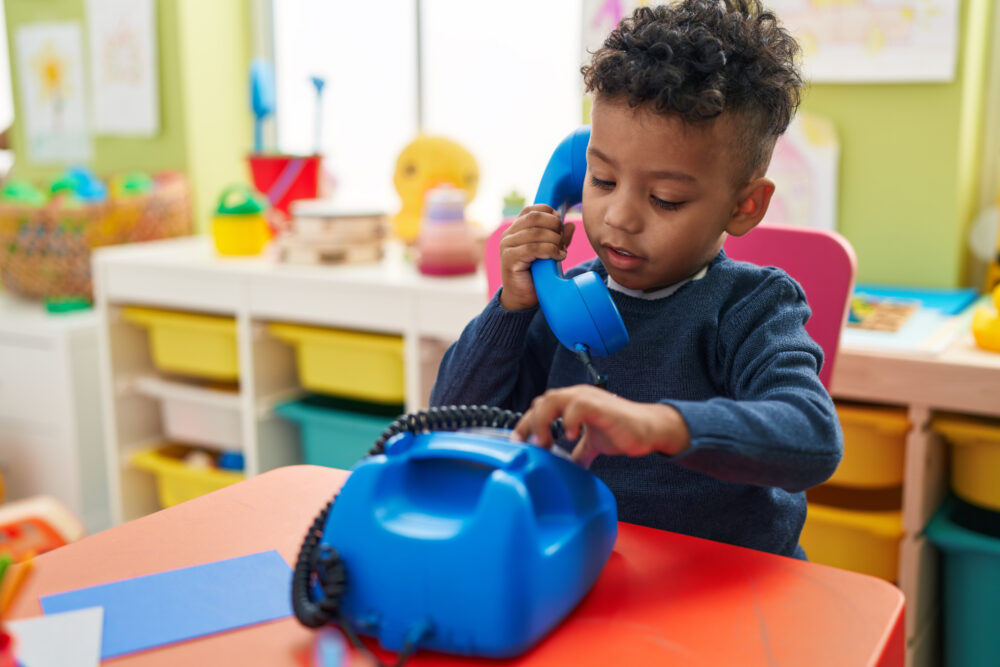Preschool-aged African-American boy playing with a telephone toy sitting on a table.