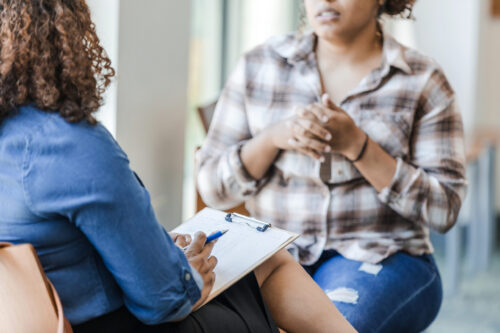 Woman in the foreground holds a clipboard and listens as another woman shares her problems. (Photo by SDI Productions, iStock)