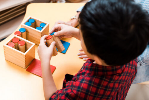 Selective focus of young child and teacher playing wooden game at desk, overhead view.