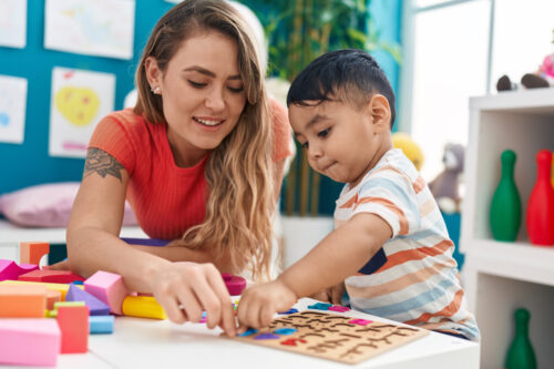 Teacher and toddler sitting at a low table, playing with a math puzzle game (Photo by Krakenimages.com, Adobe Stock)