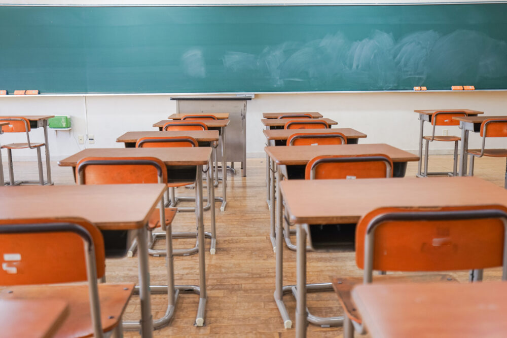 Desks facing a chalkboard in an empty classroom.