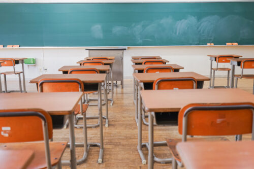 Desks facing a chalkboard in an empty classroom.