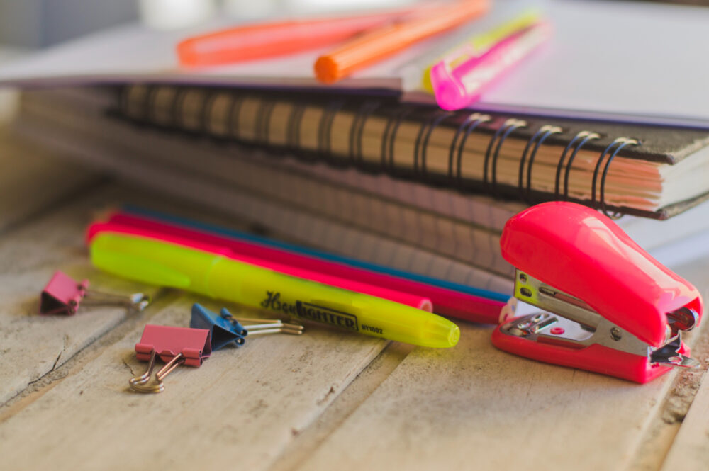 Stack of notebooks with scattered highlighters, pens, and a mini stapler.