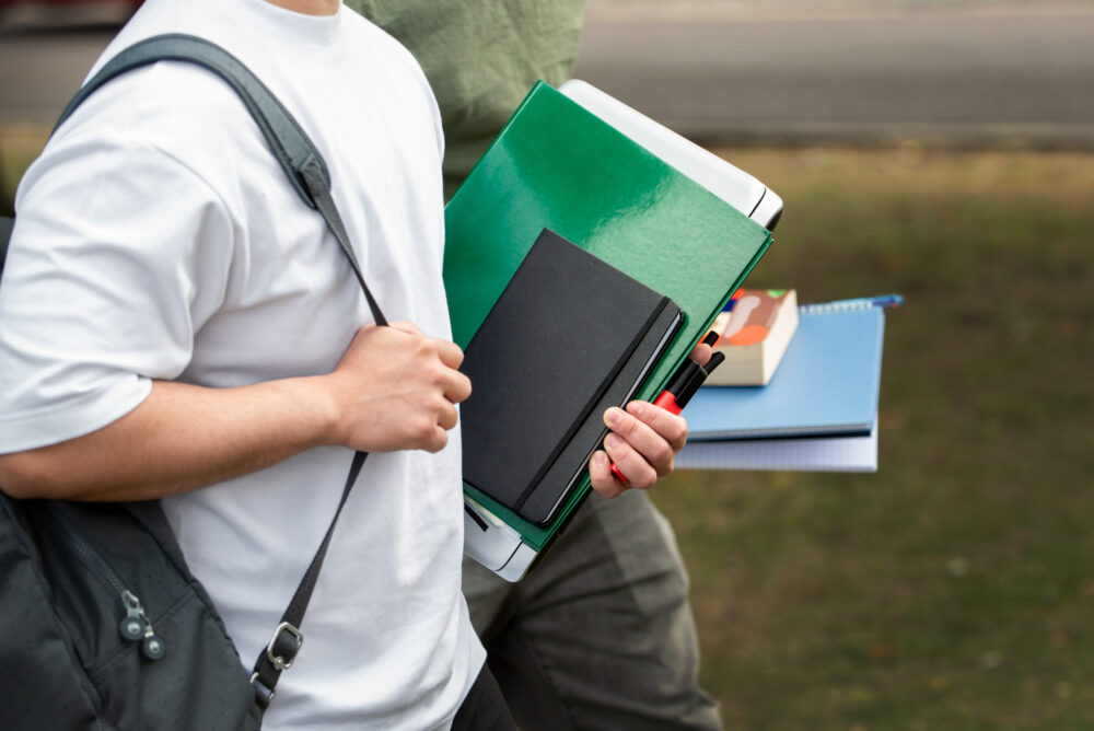 Midsection of two students walking outside, carrying school supplies