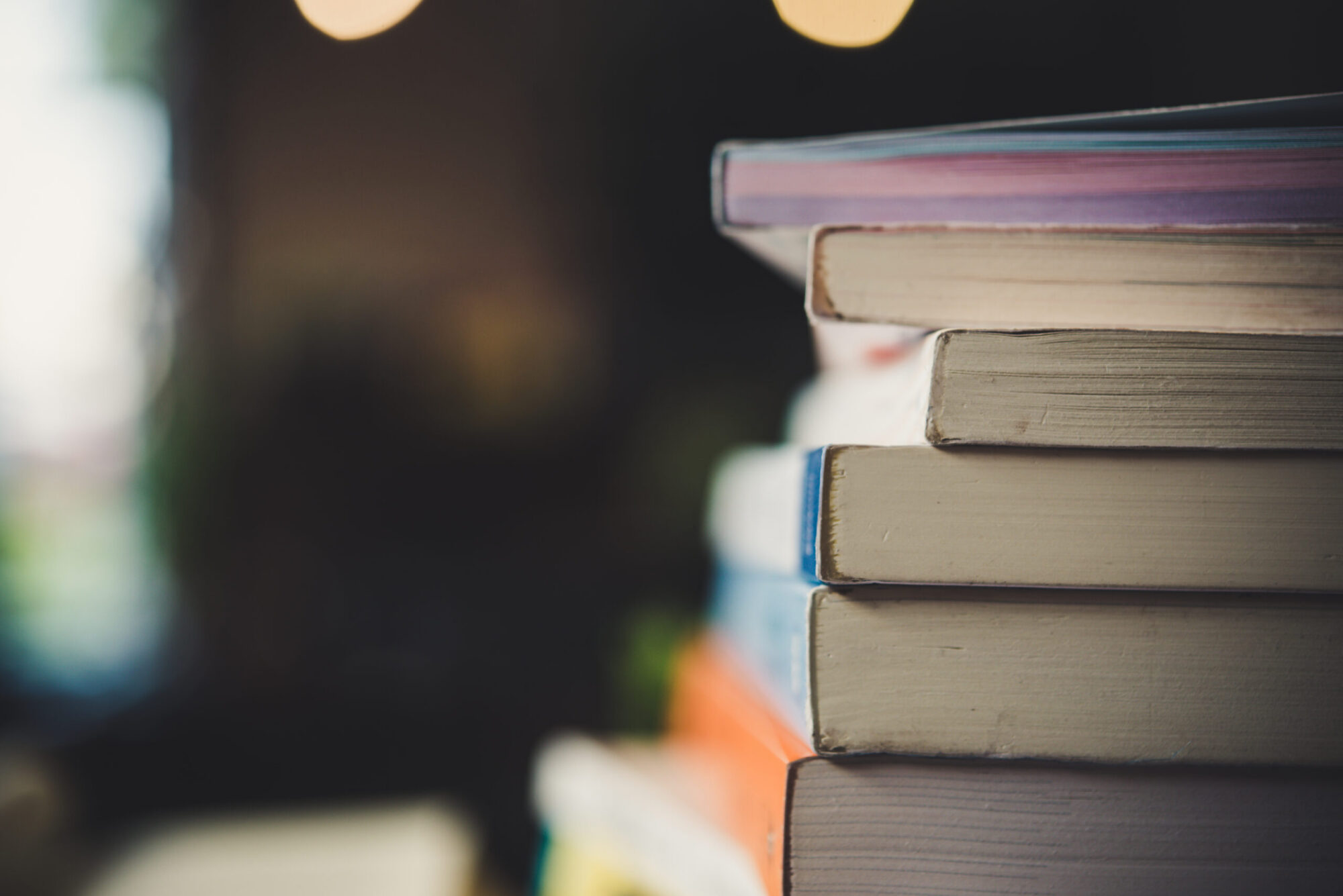 Piles of books on table over blurred library background. (Photo by Johnstocker, Adobe Stock)