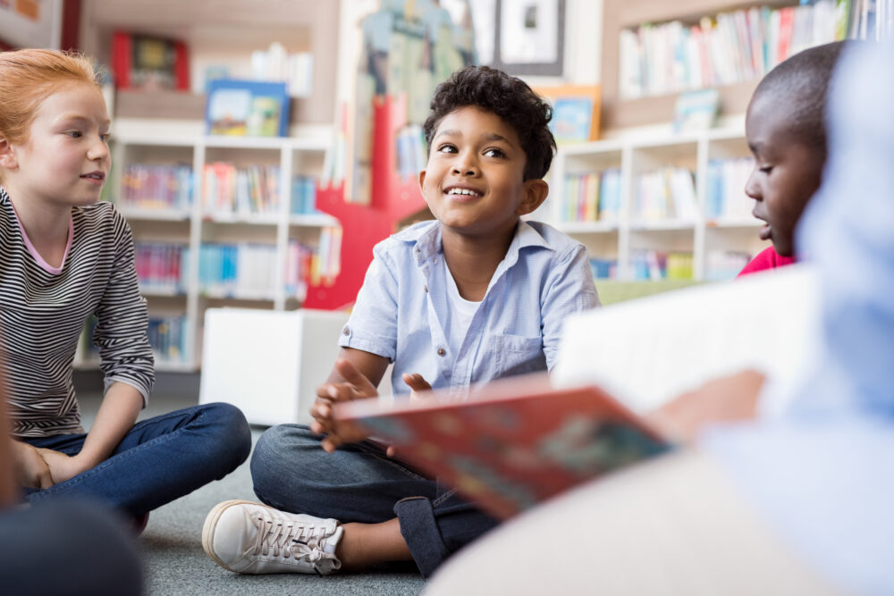 Multiethnic group of elementary schoolers sitting on floor of library, listening a story.