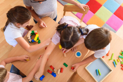 Preschool teacher with children playing with colorful wooden blocks, viewed from above