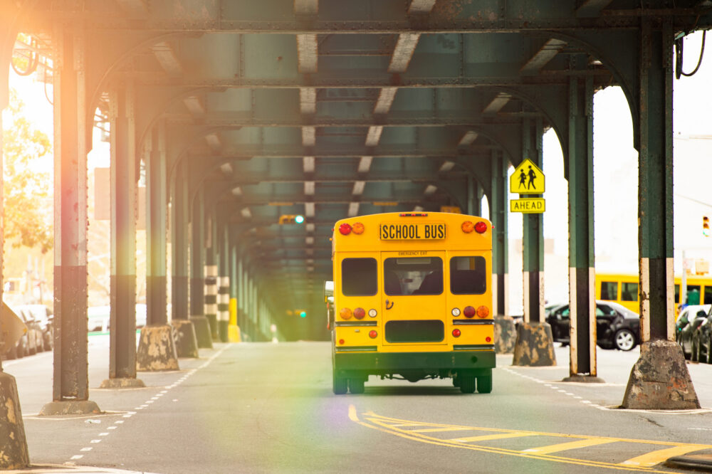 A school bus is passing under the railway bridge in the Bronx