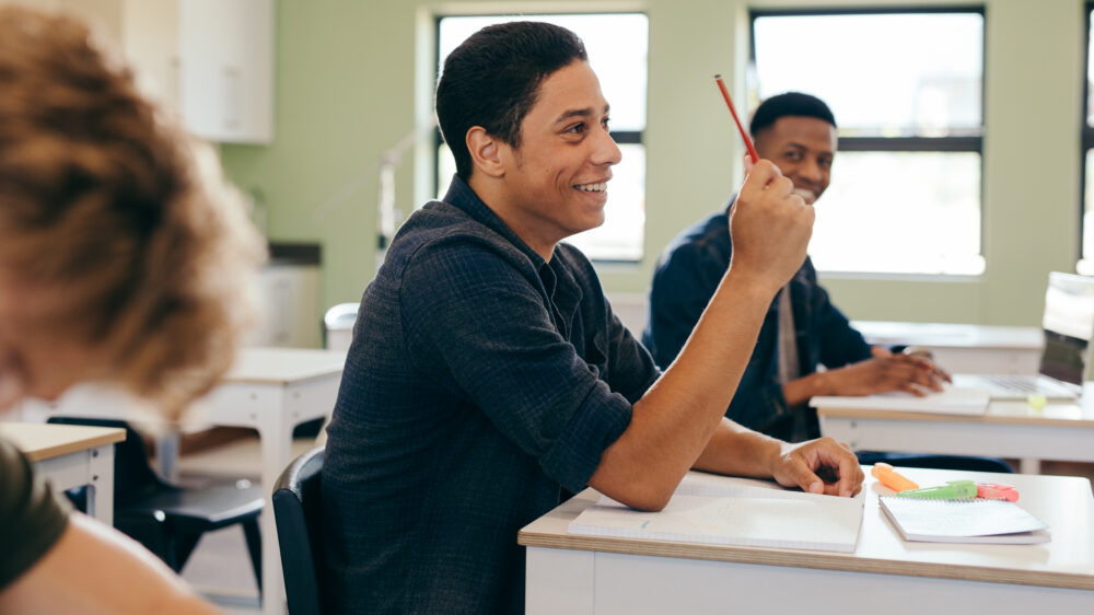 Male student sitting in the class and raising hand up to ask question during lecture. (Photo by Jacob Lund, Adobe Stock)