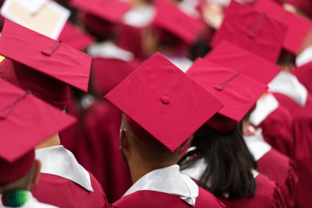 Rows of high school graduates in caps and gowns, viewed from behind. (Photo by Mat Hayward, Adobe Stock)